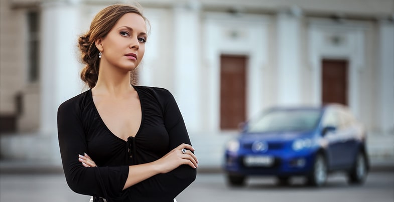  Women standing with arms folded her blue car in the background